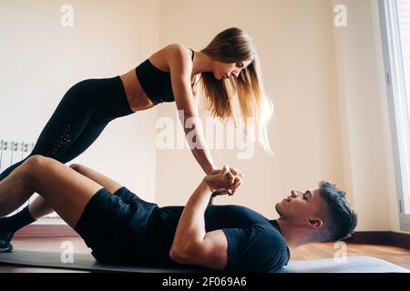Full body side view of determined man and Woman wearing sportive clothes performing difficult yoga position while practicing at home Stock Photo