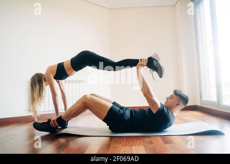 Full body side view of determined man and Woman wearing sportive clothes performing difficult yoga position while practicing at home Stock Photo