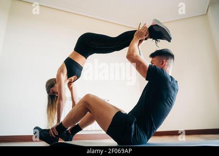 Full body side view of determined man and Woman wearing sportive clothes performing difficult yoga position while practicing at home Stock Photo