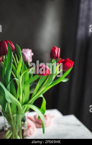 Glass vase with red tulips on the table by the window Stock Photo