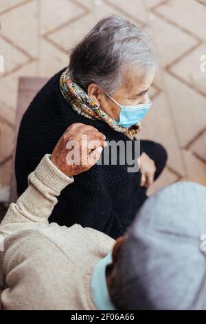 From above view of elderly couple sitting on a park bench while the husband puts his hand on his wife's shoulder in a gesture of love Stock Photo