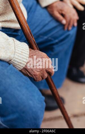 Anonymous senior person holding cane while sitting on park bench Stock Photo