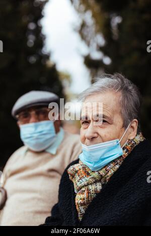 Side view of an elderly couple wearing face mask on the street as they look at the camera on a winter afternoon Stock Photo