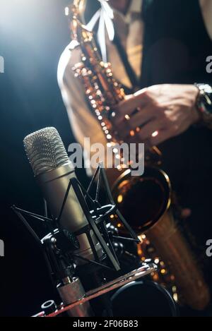 Crop unrecognizable male musician in classy outfit standing near microphone and playing alto saxophone during jazz concert Stock Photo