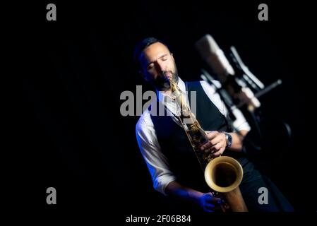 Crop of male musician in classy outfit standing near microphone and playing alto saxophone during jazz concert Stock Photo