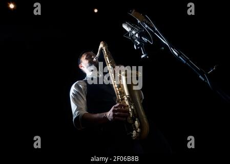 From below crop of male musician in classy outfit standing near microphone and playing alto saxophone during jazz concert Stock Photo