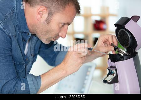 man repairing coffee machine by screwdriver in kitchen Stock Photo