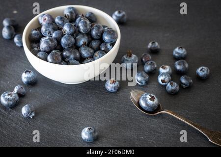 Fresh and healthy blueberries in a bowl and scattered on a black stone countertop. Place for your own inscription Stock Photo