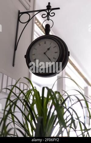 selective focus of an antique round wall clock with Roman numerals and black border placed on the wall by an iron or wrought iron support on a hotel w Stock Photo
