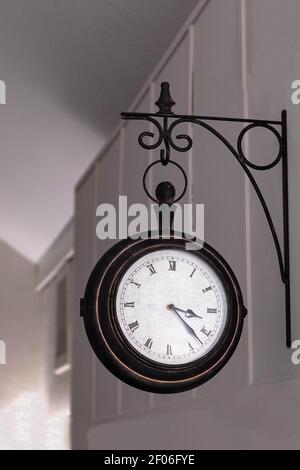selective focus of an antique round white wall clock with black border and Roman numerals on the wall of a hotel or lobby. Stock Photo