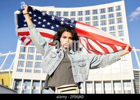 Confident Afro American woman standing on street holding flag of United States. Stock Photo