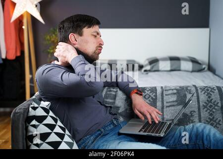 Man employee after accident working at home behind laptop and feels pain in neck, uses black neck collar support. Male with neck injury freelance Stock Photo