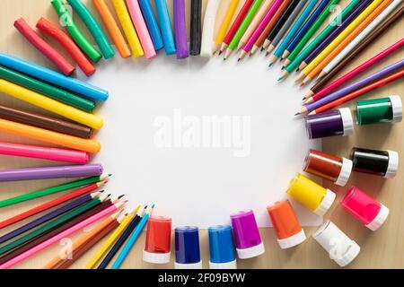 Group of bright art supplies on the desk with blank whte paper and copy space in the middle. Stock Photo