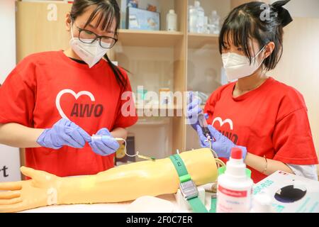 24 February 2021, Saxony, Auerbach (vogtland): Vietnamese Tuoi Phung (l) and Oanh Nguyen practice drawing blood on a training arm in the training room of Arbeiterwohlfahrt Vogtland (AWO). Three young women came to Vogtland from their home country Vietnam for training in 2017. This is now finished - since the beginning of March, they have been working for the AWO as skilled nursing staff. These are in short supply and the need is growing steadily due to the aging population. Four years ago, they were the first, now almost half of the trainees in the field of care at the social association come Stock Photo