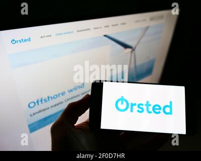 High angle view of person holding cellphone with logo of Danish power company Ørsted AS on screen in front of webpage. Focus on phone display. Stock Photo