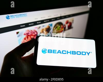 Person holding cellphone with logo of US fitness and media company Beachbody LLC on screen in front of business webpage. Focus on phone display. Stock Photo