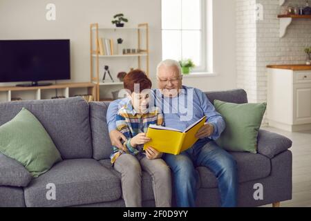 Happy grandfather reading book to his grandson while sitting on sofa in the living-room Stock Photo