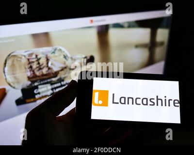 Person holding smartphone with logo of insurance company  Lancashire Insurance Group on screen in front of website. Focus on phone display. Stock Photo