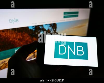 Person holding smartphone with logo of Norwegian financial services company DNB ASA on screen in front of website. Focus on phone display. Stock Photo