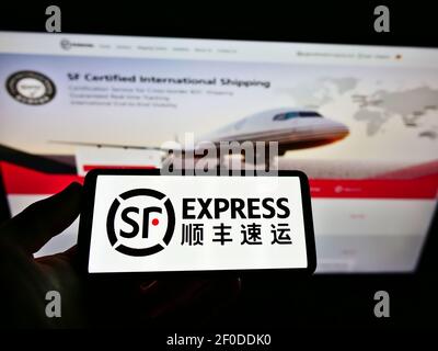 Person holding mobile phone with logo of Chinese logistics company SF Express (Group) Co. Ltd. on screen in front of webpage. Focus on phone display. Stock Photo