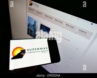 Person holding mobile phone with logo of Malaysian gloves producer Supermax Corporation Berhad on screen in front of webpage. Focus on phone display. Stock Photo