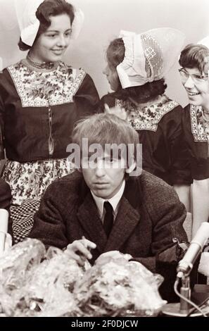 Dutch girls stand behind lead guitarist George Harrison at a Schiphol Airport press conference when The Beatles arrived in Amsterdam, Holland on June 5, 1964. Stock Photo