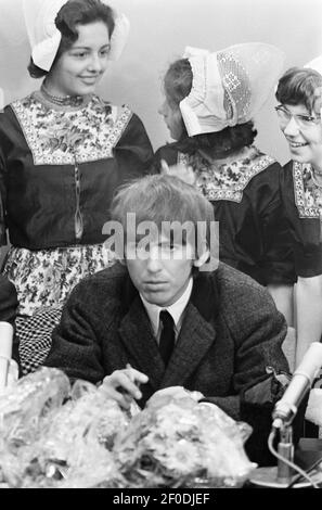 Dutch girls stand behind lead guitarist George Harrison at a Schiphol Airport press conference when The Beatles arrived in Amsterdam, Holland on June 5, 1964. Stock Photo