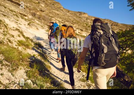 Back view of tourists with backpacks are climbing by a rocky trail in a ...