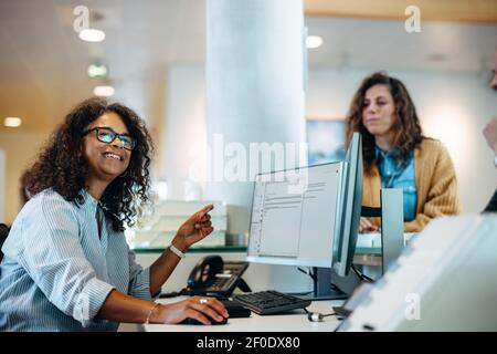 Woman working at government office reception looking away and smiling with people standing in queue at front desk. Stock Photo