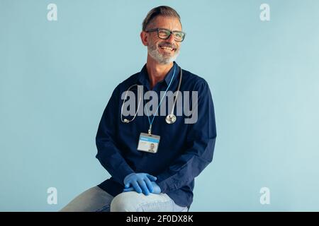 Portrait of a happy mature male doctor on blue background. General practitioner with stethoscope looking at camera and smiling. Stock Photo