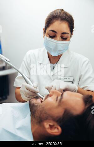 Female doctor doing dental treatment on man's teeth in the dentists chair. Female dentist wearing face mask treating a patient. Stock Photo