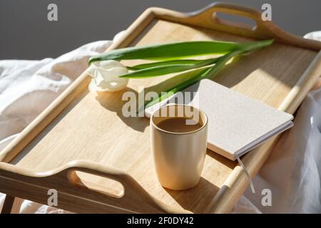 Portable wooden desk with warm cup of coffee, tulip, diary in bedroom. Hygge, Scandinavian style, lagom. Stock Photo
