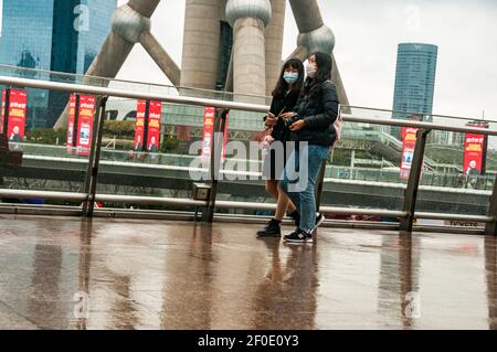 Two girls on the skywalk in front of the Oriental Pearl Tower in Shanghai’s Lujiazui, Pudong District, China on a cold rainy early spring day. Stock Photo