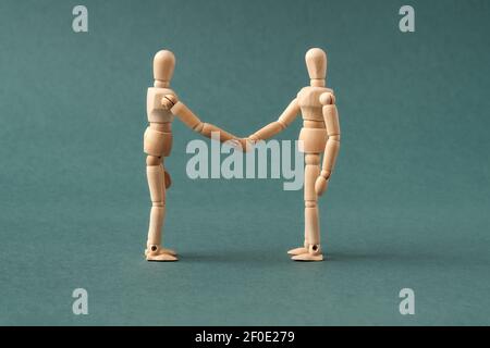 Two wooden figures shaking hands on blue background - agreement or friendship concept Stock Photo