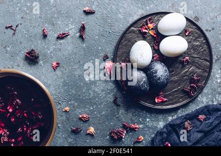 Dyed Easter eggs with marble stone effect painted with natural dye carcade tea from hibiscus flowers on dark blue concrete background. Top view. Stock Photo