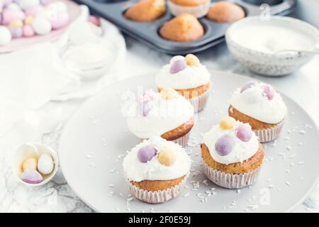 Glazed Easter cupcakes decorated with mini chocolate eggs candy on white marble background. Happy Easter Holidays. Stock Photo