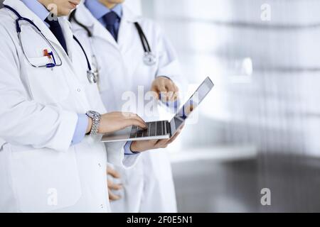 Two unknown doctors with stethoscopes discuss medical exam resoults, while standing at hospital office. Physicians using a laptop for checking up Stock Photo