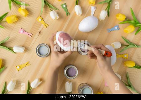 Female hands holding brush painting easter eggs on wooden table background flat lay composition Stock Photo