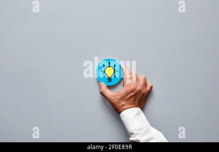 Businessman hand holding a blue badge with light bulb icon. Creativity, idea, innovation or brainstorming in business concept. Stock Photo