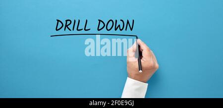 Businessman hand writing the business buzzword drill down on blue background. Going deep into the specific details of the information for analysis in Stock Photo