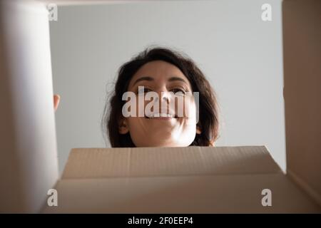 Curious millennial female face look inside cardboard box postal parcel Stock Photo