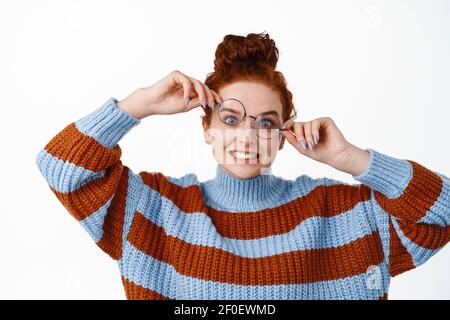 Happy and positive ginger girl with hair combed in hairbun, playing with glasses and making funny faces, trying new eyewear frame to match her face Stock Photo