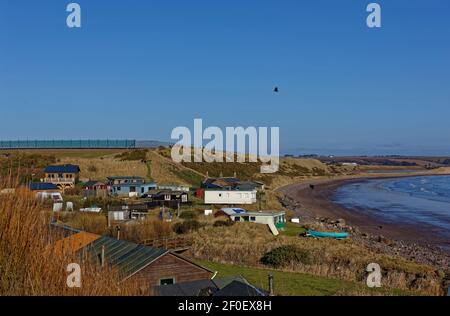 The small community of Korbie Knowe sheltered below the Cliffs at the southern end of lunan Bay on the East Coast of Scotland on a sunny morning in Ma Stock Photo