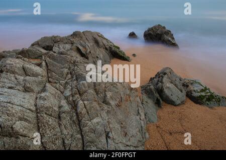 Long exposure with Sahara Sand in Mediterranean Sea and rocks on the beach in Catalunya, Spain Stock Photo