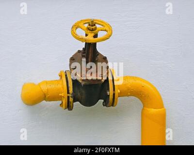 Old gas valve attached on the pipe that goes into the vertical house wall Stock Photo