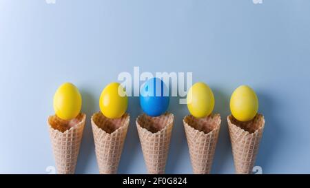 Yellow eggs and one blue in waffle cones lie on a blue horizontal background. Easter background concept flat lay, copy space, selective focus Stock Photo