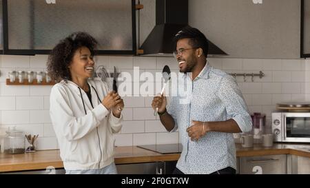 Overjoyed African American couple having fun with kitchenware in kitchen Stock Photo