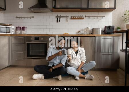 Overjoyed African American couple drinking tea, sitting on kitchen floor Stock Photo
