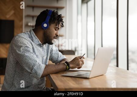 Side view African American man wearing headphones taking notes Stock Photo