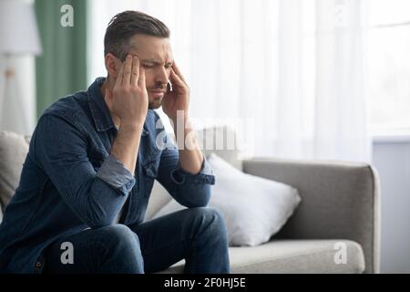 Stressed man having headache, sitting on sofa at home Stock Photo